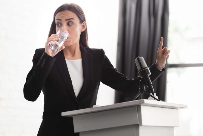 девушка пьет воду, выступая перед аудиторией